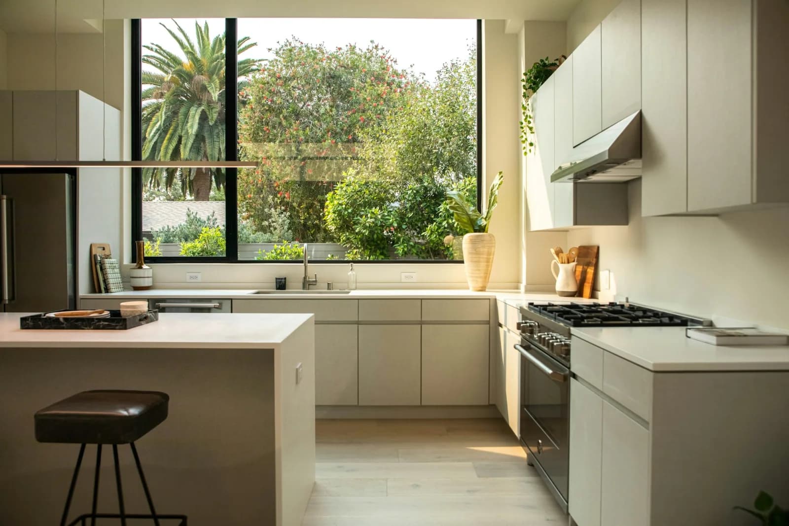 Cuisine résidentielle contemporaine aux armoires beige clair, îlot central et grande fenêtre donnant sur un jardin verdoyant