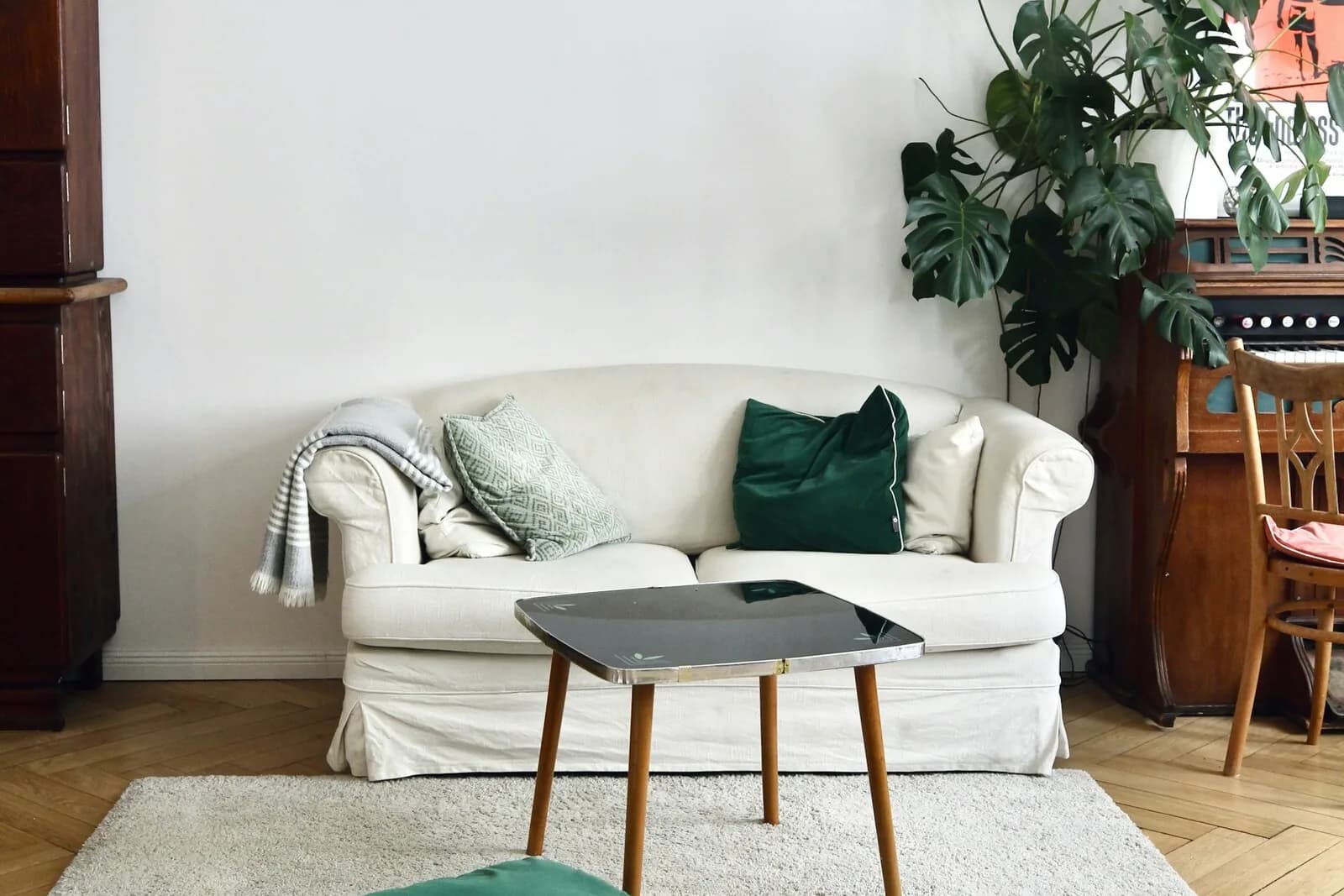 Salon lumineux et rangé avec canapé blanc, coussins vert sapin, tapis clair et parquet en chevrons